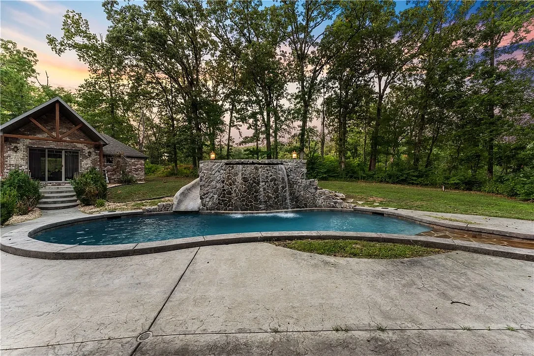 Pool with stone waterfall surrounded by trees at sunset